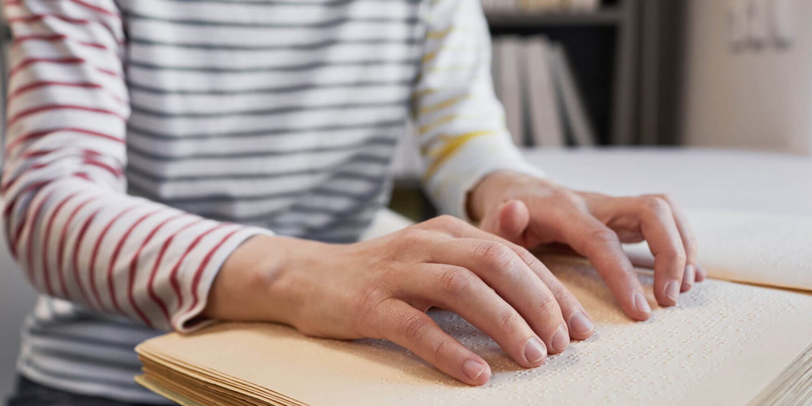 Persoon met gestreepte trui leest met twee handen een braille boek